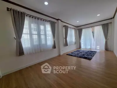Spacious living room with large windows and elegant curtains, featuring wooden flooring and a cozy rug.
