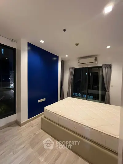 Modern bedroom with large windows and blue accent wall in a stylish apartment.