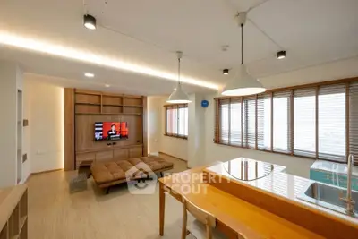 Modern living room with open kitchen, featuring sleek wooden furniture and ample natural light.