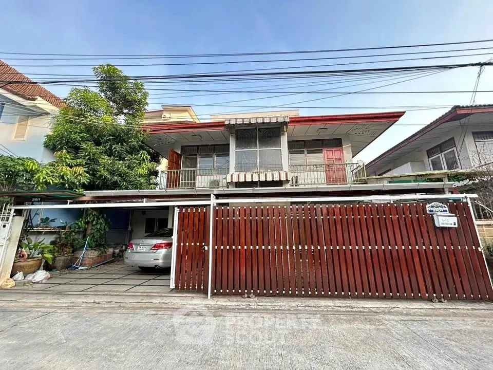 Charming two-story house with gated driveway and lush greenery in a serene neighborhood.