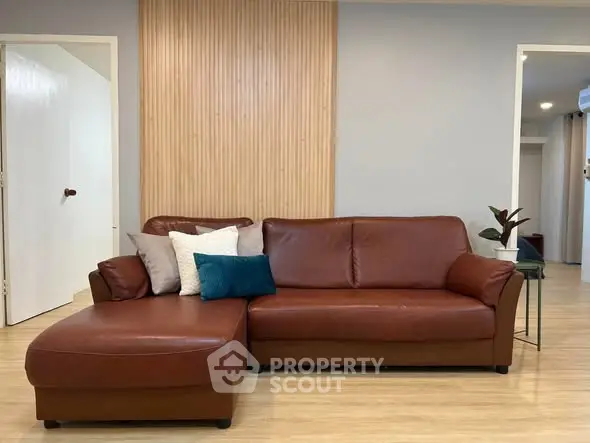 Modern living room with stylish brown leather sofa and wooden accent wall.