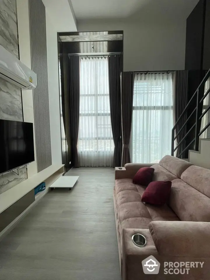 Modern living room with high ceiling and large windows, featuring a stylish sofa and wall-mounted TV.