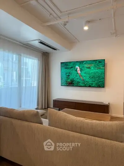 Modern living room with cozy sofa and large TV, featuring stylish decor and natural light.