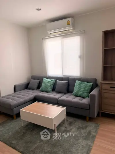 Cozy living room with modern gray sofa, green cushions, and air conditioning, perfect for relaxation.