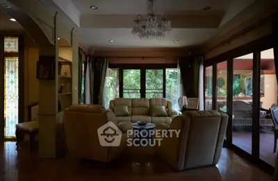 Luxurious living room with elegant chandelier and garden view, featuring plush seating and large windows.
