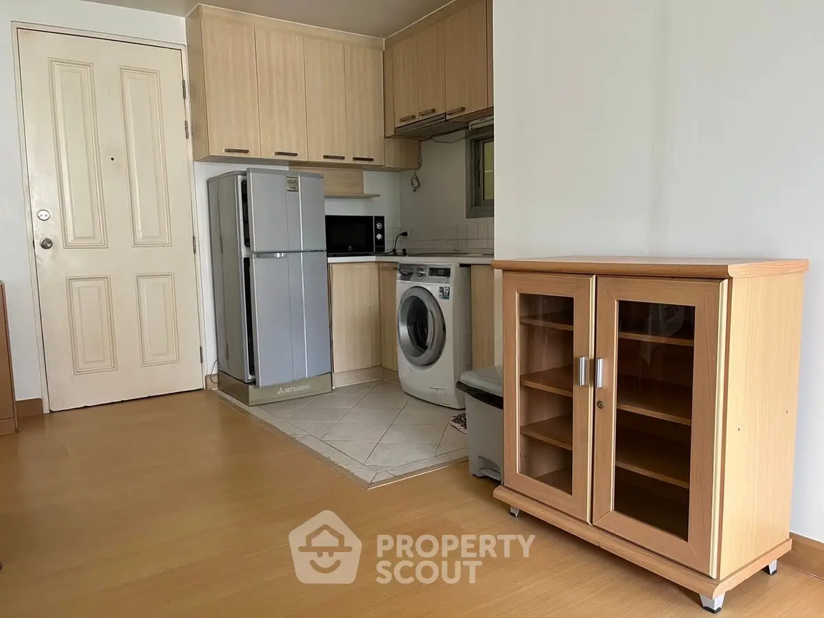 Compact kitchen with fridge, washing machine, and microwave in modern apartment.