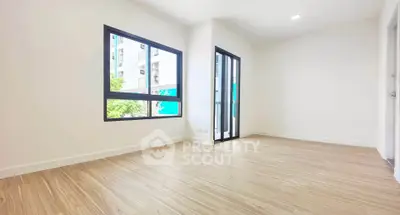 Spacious empty room with large windows and wooden flooring in modern apartment.