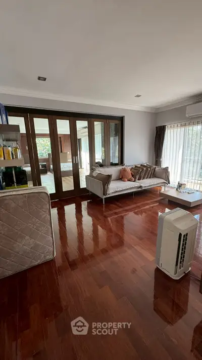 Spacious living room with wooden flooring and modern furniture, featuring large windows for natural light.