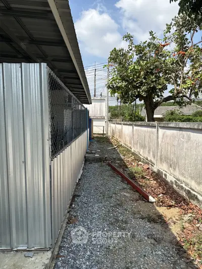 Narrow gravel pathway beside a metal fence and tree in residential area
