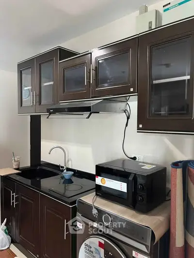 Modern kitchen with dark cabinets, microwave, and washing machine, ideal for compact living spaces.