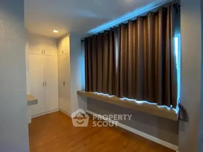 Spacious room with wooden flooring and large window with curtains