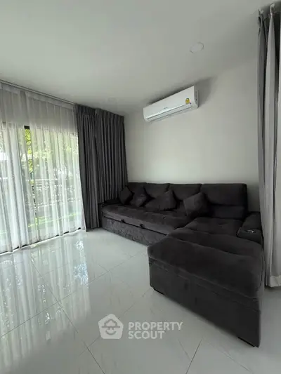 Modern living room with sleek gray sofa and air conditioning, featuring large windows with elegant curtains.