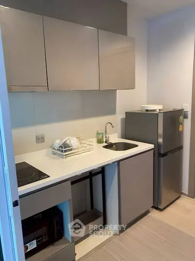 Modern compact kitchen with sleek cabinets and stainless steel fridge in a cozy apartment.