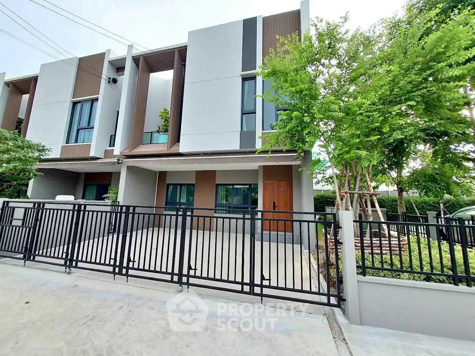 Modern townhouse exterior with sleek design and gated driveway, surrounded by lush greenery.