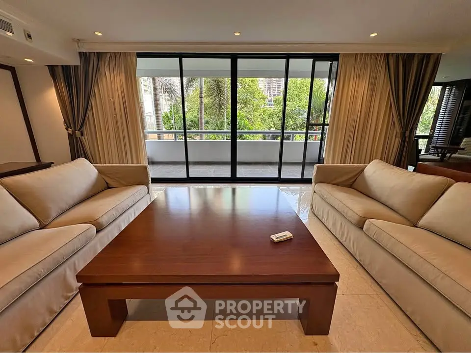 Spacious living room with elegant sofas and large windows opening to a lush balcony view.