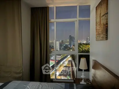 Cozy bedroom with large windows offering a stunning city view, complemented by warm lighting and tasteful decor, perfect for urban living.