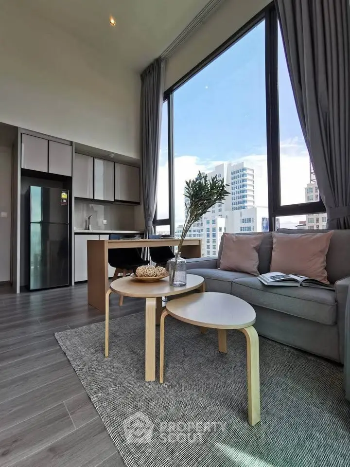 Modern living room with large windows and city view, featuring stylish furniture and open kitchen layout.