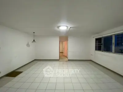 Spacious empty room with tiled flooring and large window, ideal for customization.