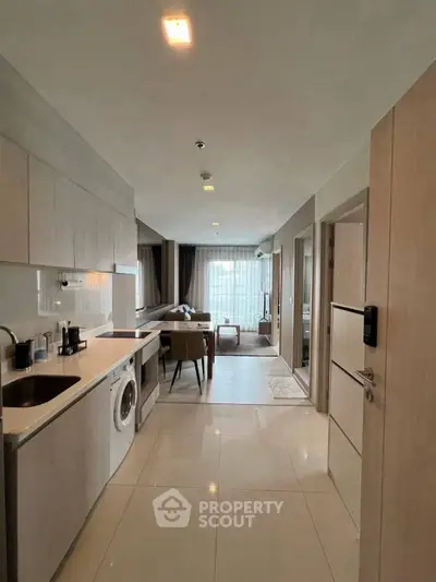 Modern open-layout apartment with sleek kitchen and cozy living area, featuring a washing machine.