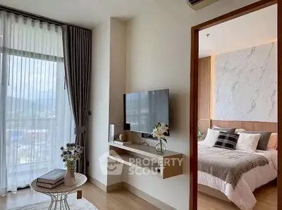 Modern living room with TV and cozy bedroom view, featuring elegant decor and natural light.