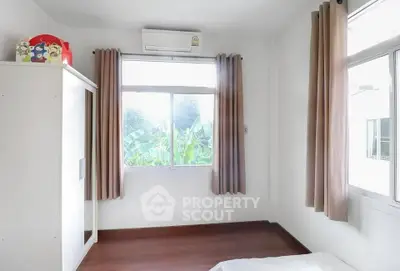Bright bedroom with large window and air conditioning, featuring a wardrobe and wooden flooring.