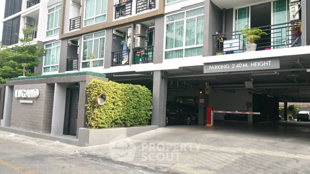 Modern condominium entrance with parking area and lush greenery.