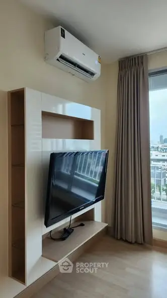 Modern living room with wall-mounted TV and air conditioning, featuring large window with city view.