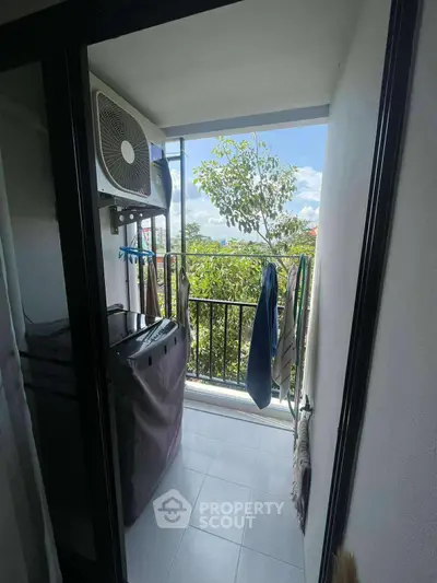 Compact balcony with laundry area and scenic view of trees and sky.