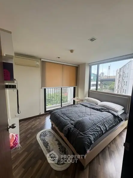 Cozy bedroom with large windows offering city views, featuring modern decor and wooden flooring.