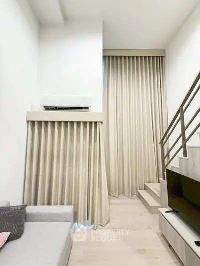 Modern living room with high ceilings, elegant curtains, and a cozy staircase leading to a loft area.