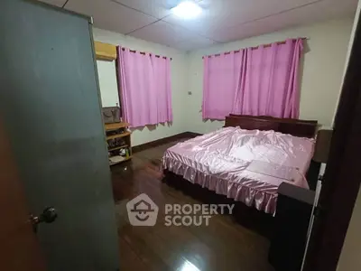 Cozy bedroom with pink curtains and bedding, wooden floor, and ample natural light.