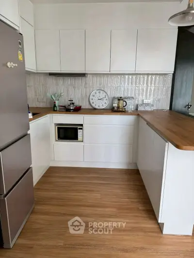 Modern kitchen with sleek white cabinets and wooden countertops, featuring a built-in microwave and stylish backsplash.