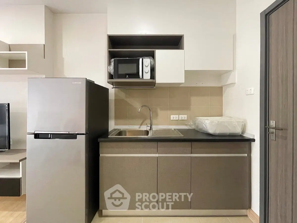 Modern kitchen with sleek cabinetry, stainless steel fridge, and built-in microwave in a stylish apartment.