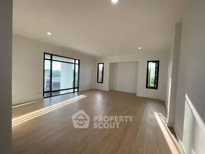 Spacious sunlit living room with large windows and wooden flooring