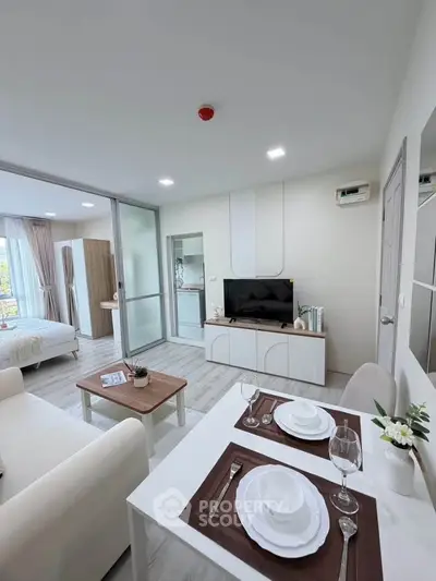 Modern open-plan living room with dining area and bedroom view, featuring sleek furniture and bright decor.