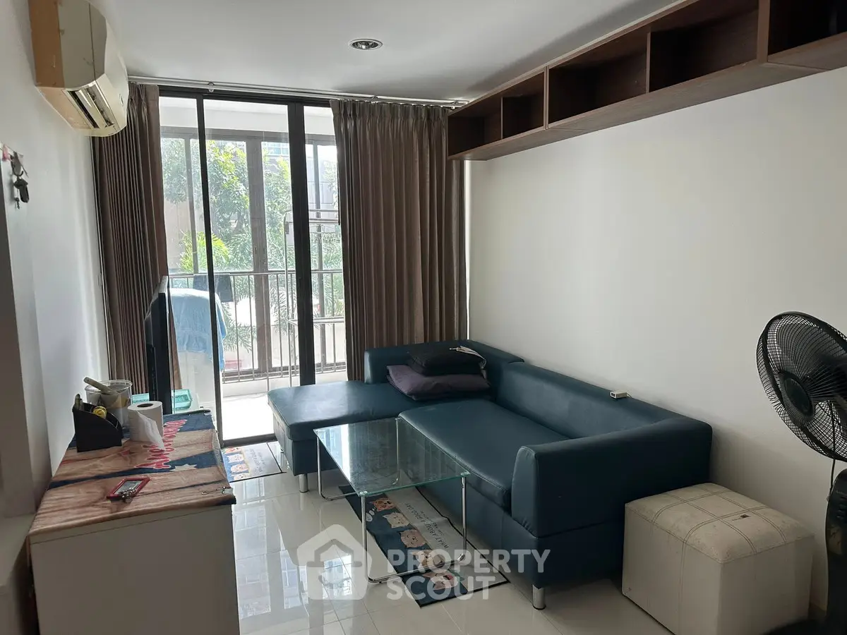 Modern living room with glass coffee table and large windows leading to balcony.