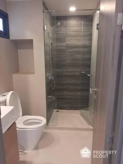 Modern bathroom with sleek glass shower enclosure and stylish dark tile walls, complemented by neutral tones for a serene ambiance.