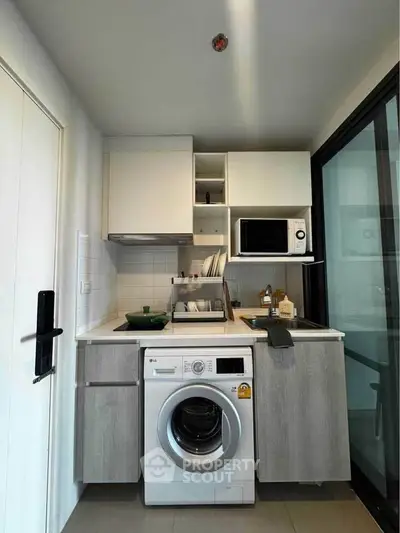 Modern compact kitchen with washing machine and microwave in sleek apartment.