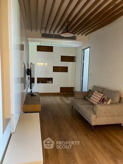 Modern living room with wooden flooring and stylish ceiling design, featuring a cozy sofa and wall-mounted TV.