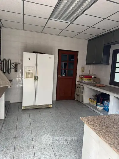 Spacious kitchen with tiled flooring, large refrigerator, and ample storage space.