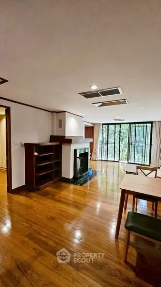 Spacious living room with wooden flooring and large windows overlooking greenery.