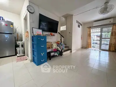 Spacious living room with modern decor and large TV, featuring tiled flooring and ample natural light.