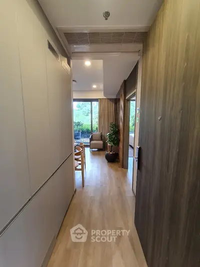 Modern apartment hallway leading to a bright living room with large windows and greenery view.