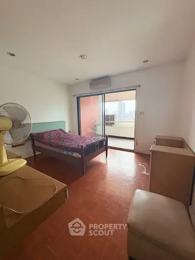 Spacious bedroom with balcony offering city views, featuring wooden flooring and modern furnishings.
