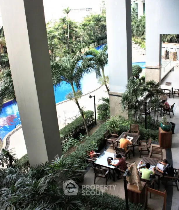 Luxurious poolside view with lush greenery and outdoor seating area in a modern residential complex.
