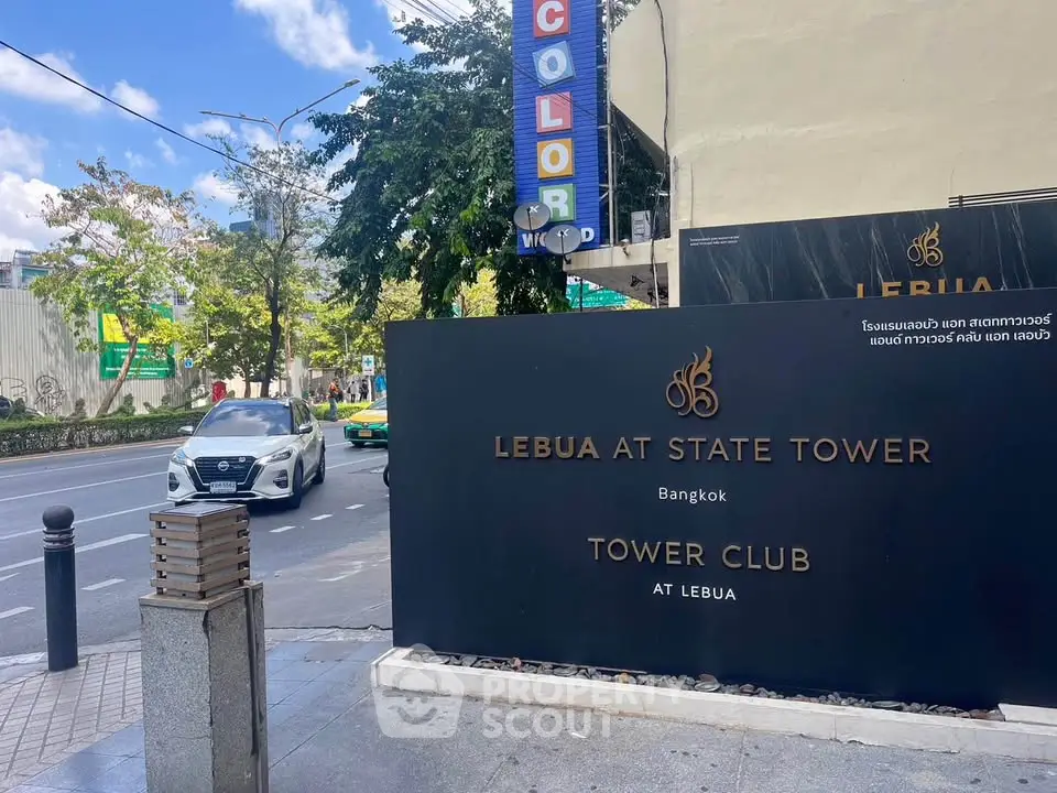 Lebua at State Tower entrance sign in Bangkok with street view and cars passing by.