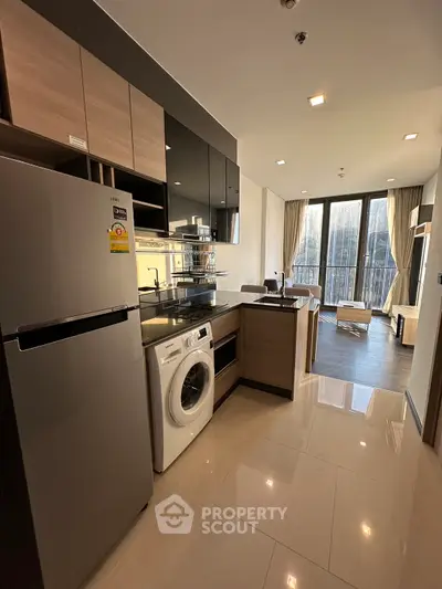 Modern kitchen with sleek appliances and open layout leading to a bright living area with large windows.