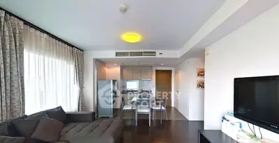 Modern living room with open kitchen and dining area, featuring sleek furniture and ample natural light.