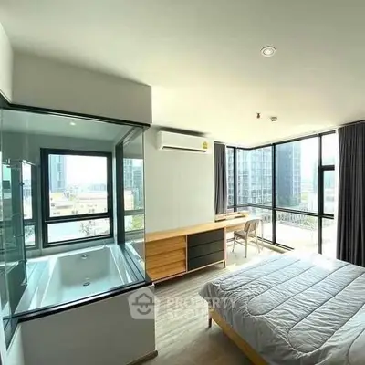 Modern bedroom with glass-enclosed bathtub and city view, featuring sleek furniture and large windows.