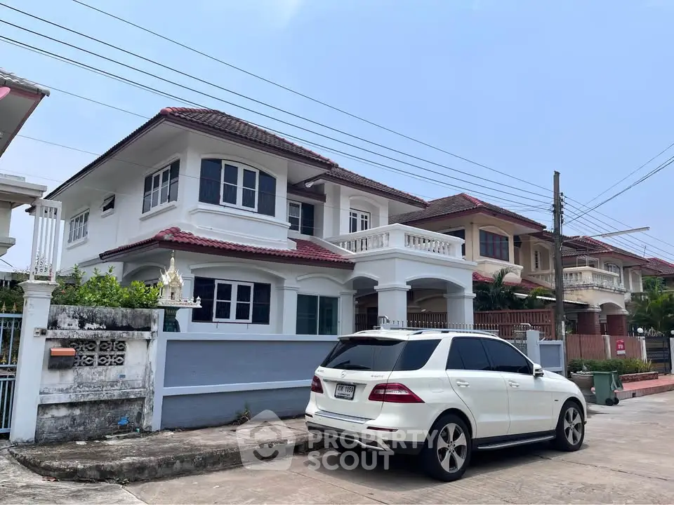Charming two-story house with red-tiled roof and white exterior, featuring a spacious driveway and elegant balcony.